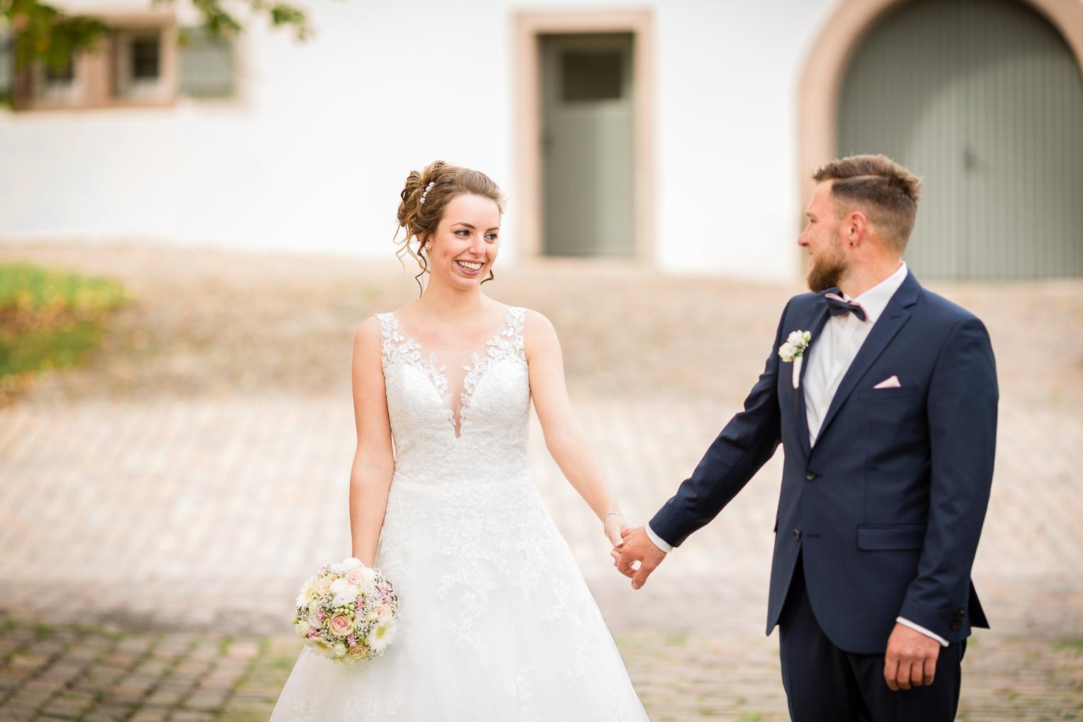 Braut mit Brautstrauß und Bräutigam spazieren Hand in Hand über Klosterhof Kirchberg