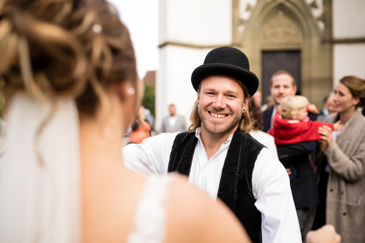 Gast mit Melone und Weste begrüßt die Braut nach der Trauung in Gruol