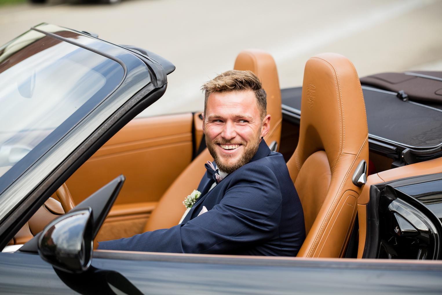 Bräutigam sitzt lachend im Cabrio nach der kirchlichen Trauung in Gruol
