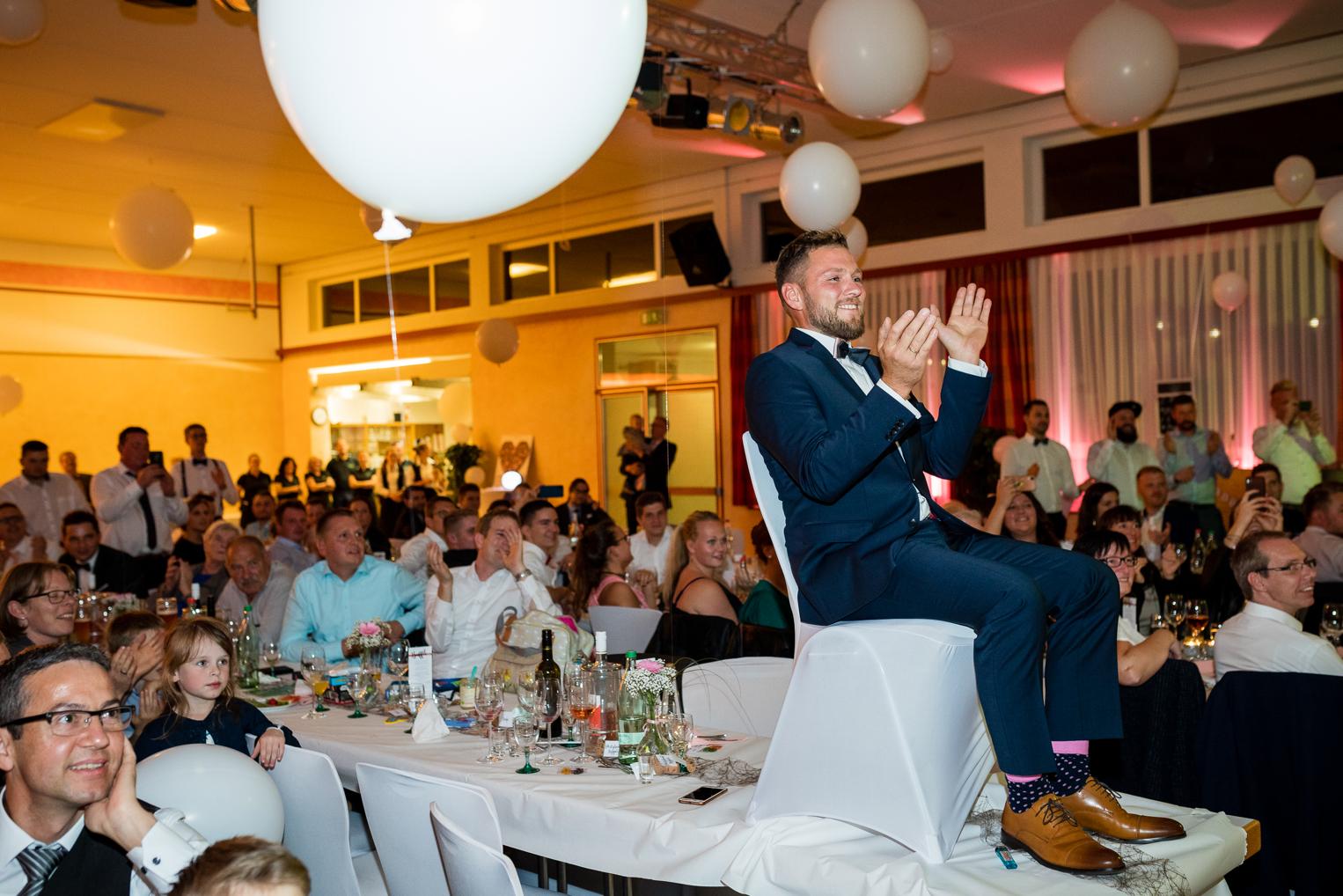 Bräutigam sitzt auf dem Tisch und applaudiert bei Hochzeitsshow in der Festhalle Gruol