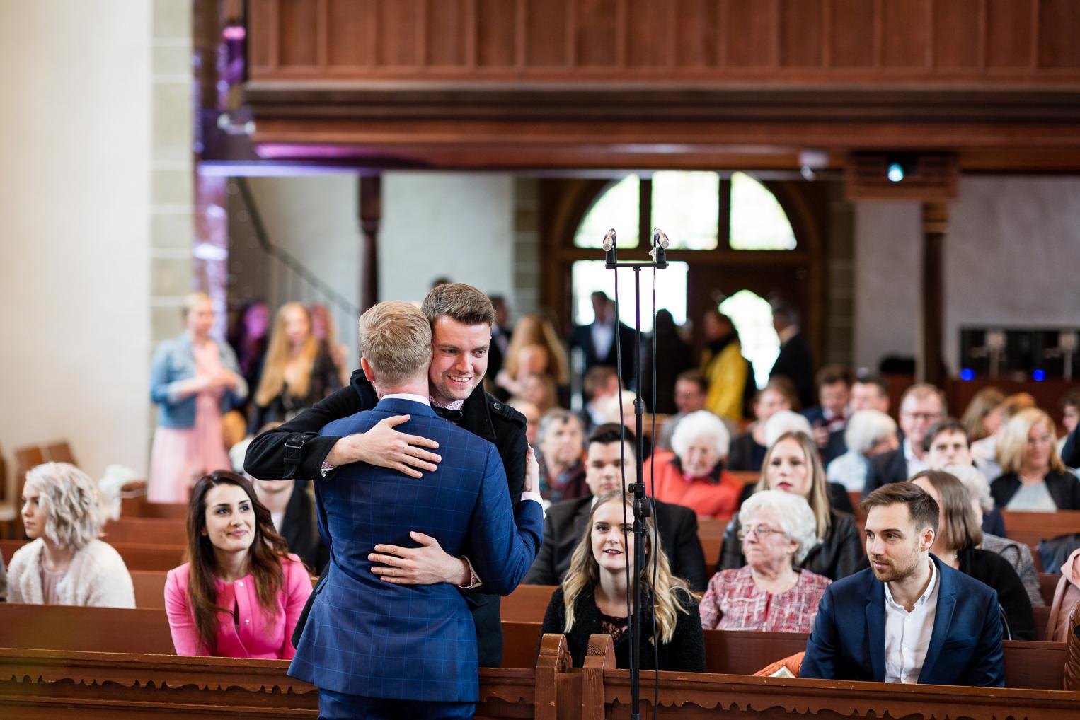 Bräutigam umarmt herzlich einen Gast in der Kirche Gärtringen vor der Hochzeitsfeier