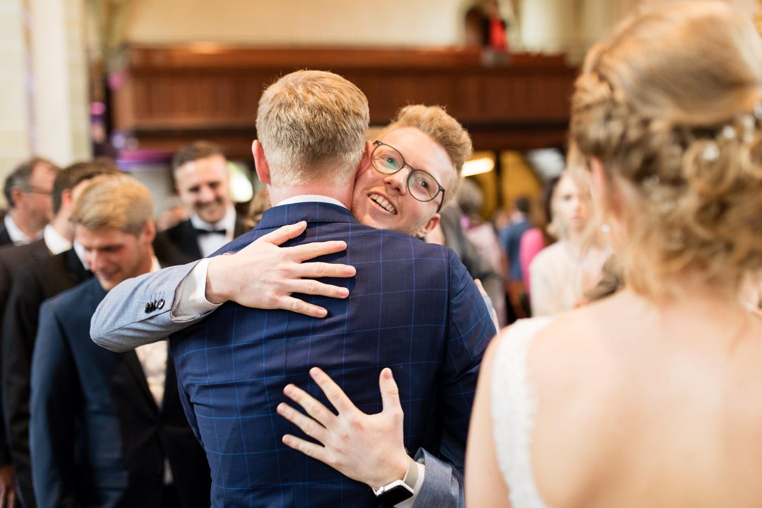 Bräutigam umarmt lachend einen Gast beim Empfang nach der Hochzeit in der Kirche Gärtringen