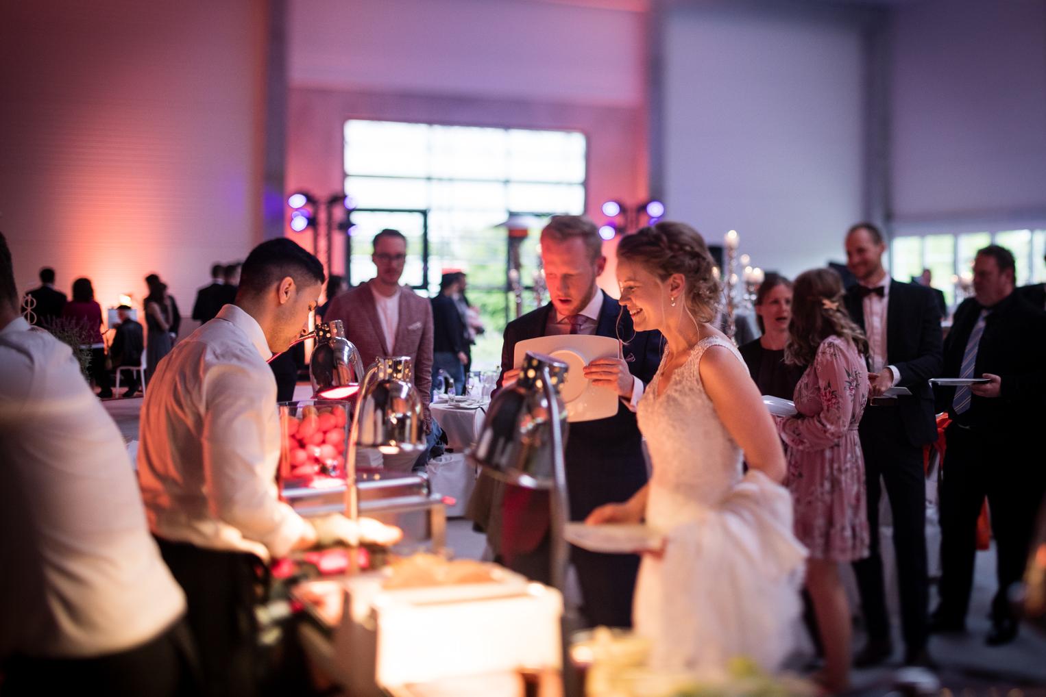 Braut und Bräutigam lachen an der Burger-Station beim Hochzeitsempfang