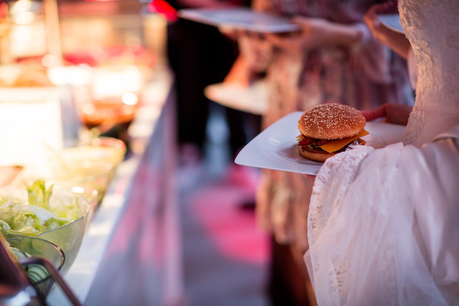 Braut hält einen Burger auf dem Teller beim Hochzeitsempfang – entspanntes Catering