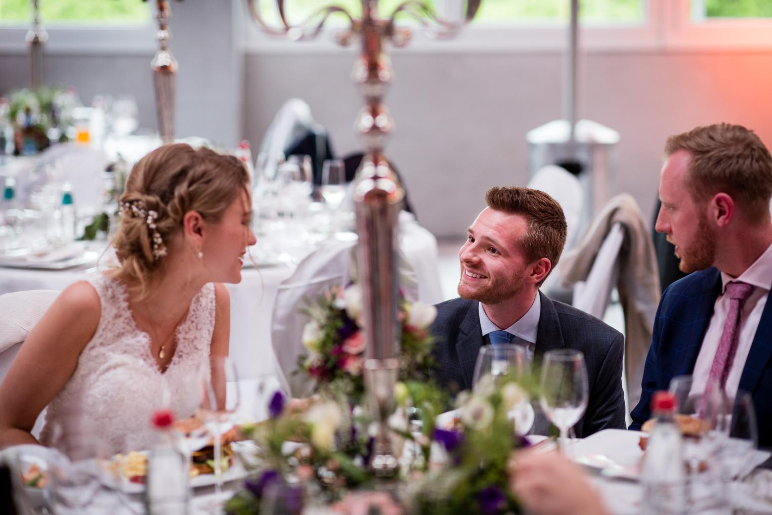 Braut und Gäste unterhalten sich lebhaft am festlich gedeckten Tisch beim Hochzeitsessen