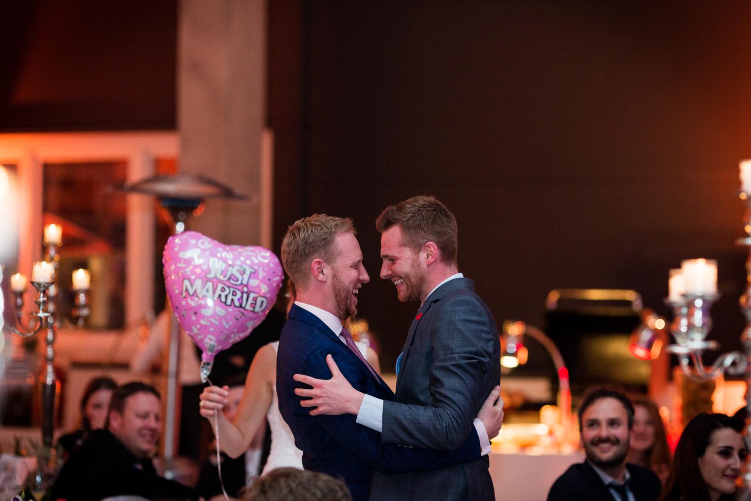 Bräutigam lacht herzlich mit einem Freund bei der Feier, „Just Married“-Ballon im Hintergrund