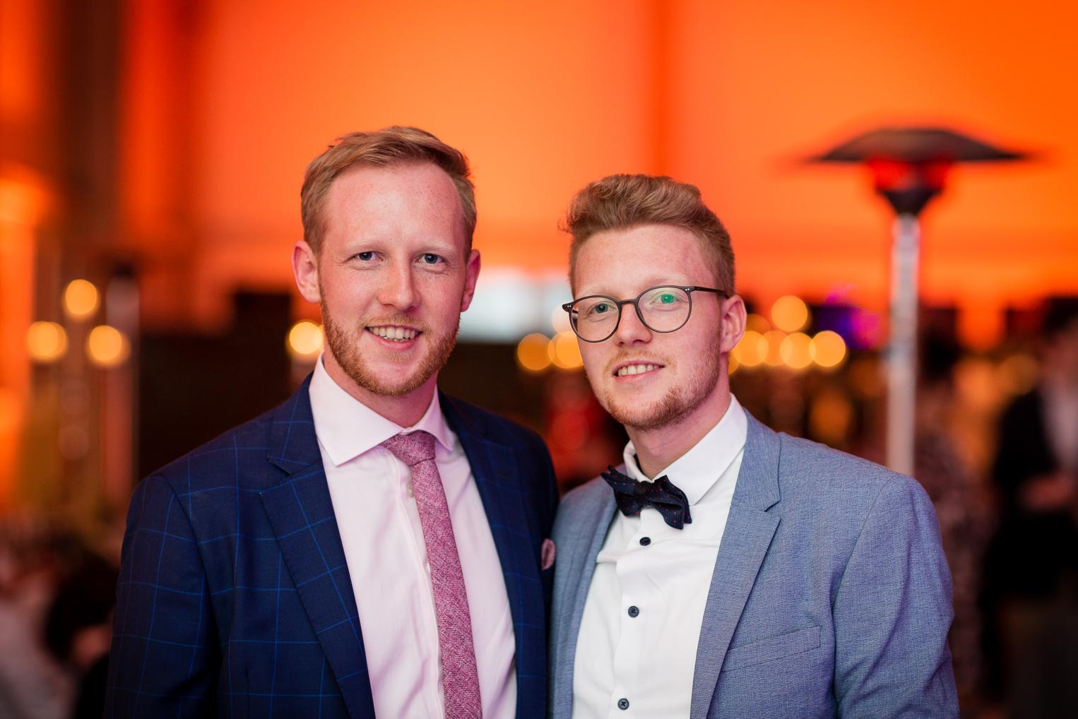 Bräutigam und Gast posieren lächelnd beim Hochzeitsempfang mit warmer Lichtstimmung