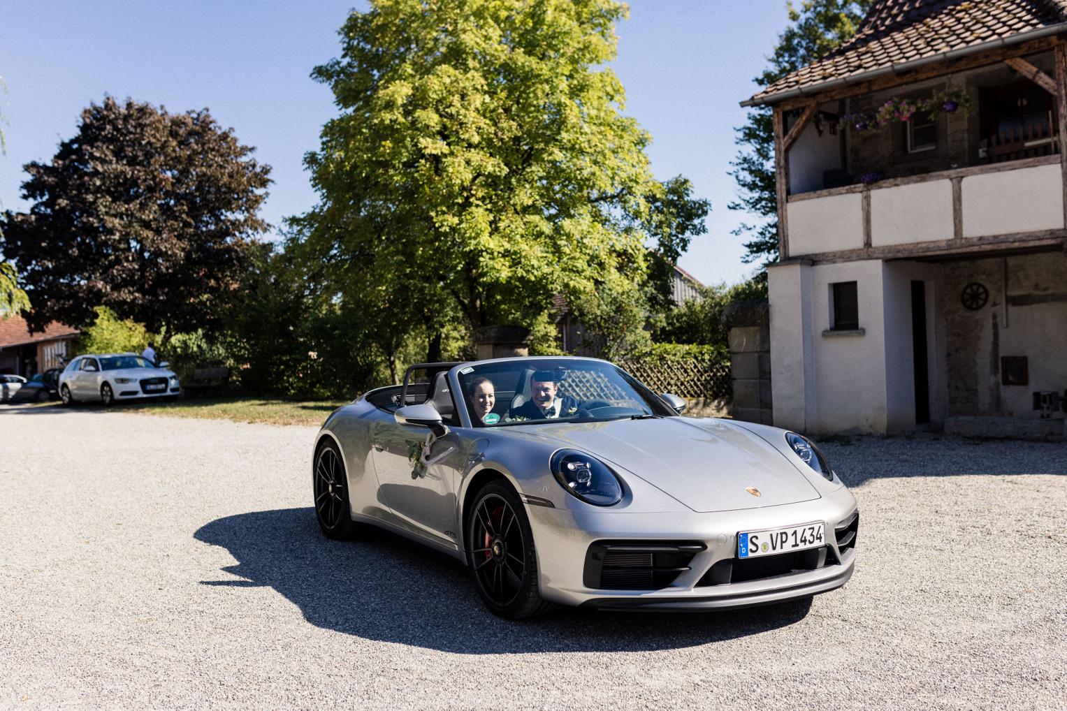 Brautpaar fährt im Porsche Cabrio vor dem Landgut vor