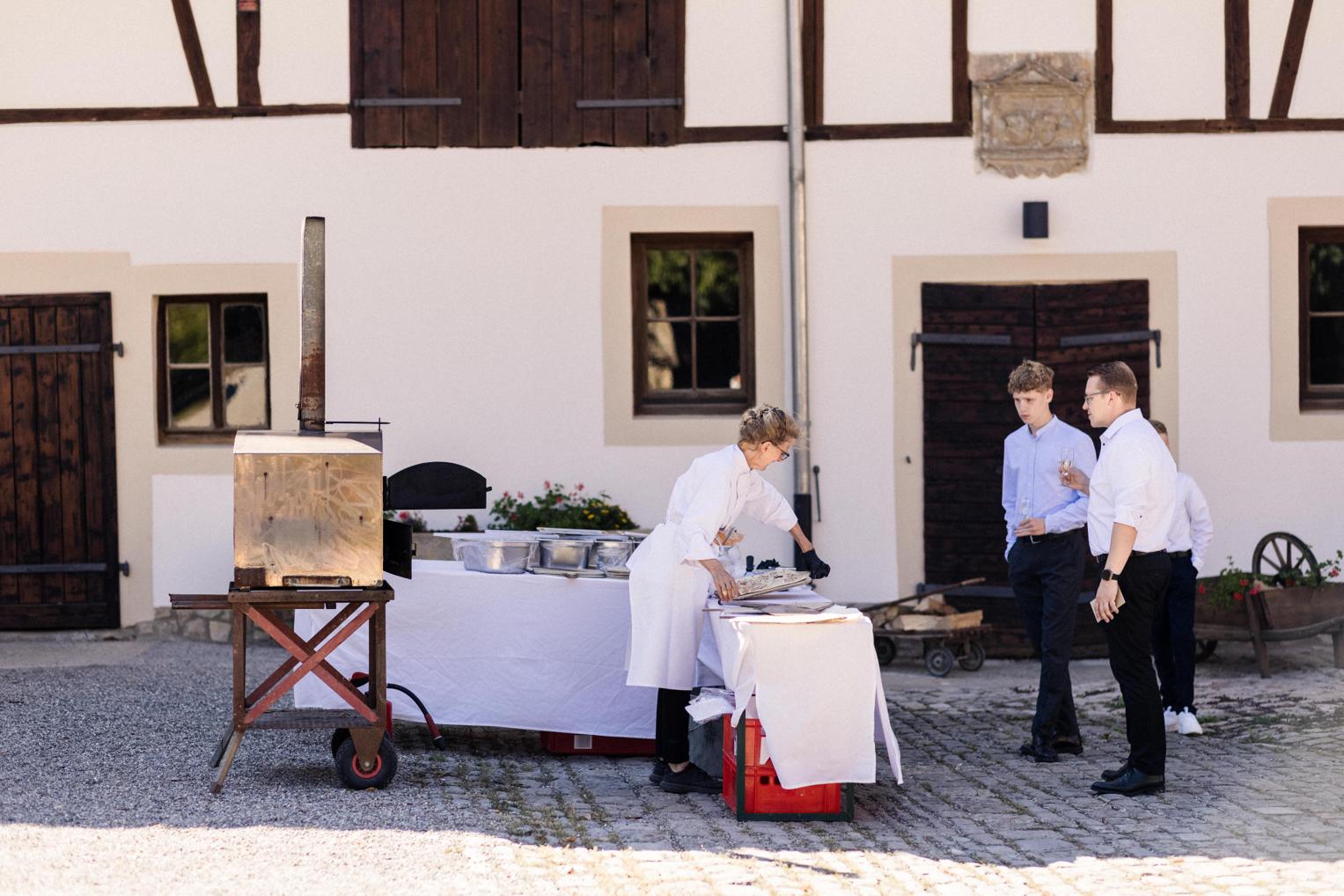 Catering-Team bereitet im Innenhof Speisen am Holzofen zu