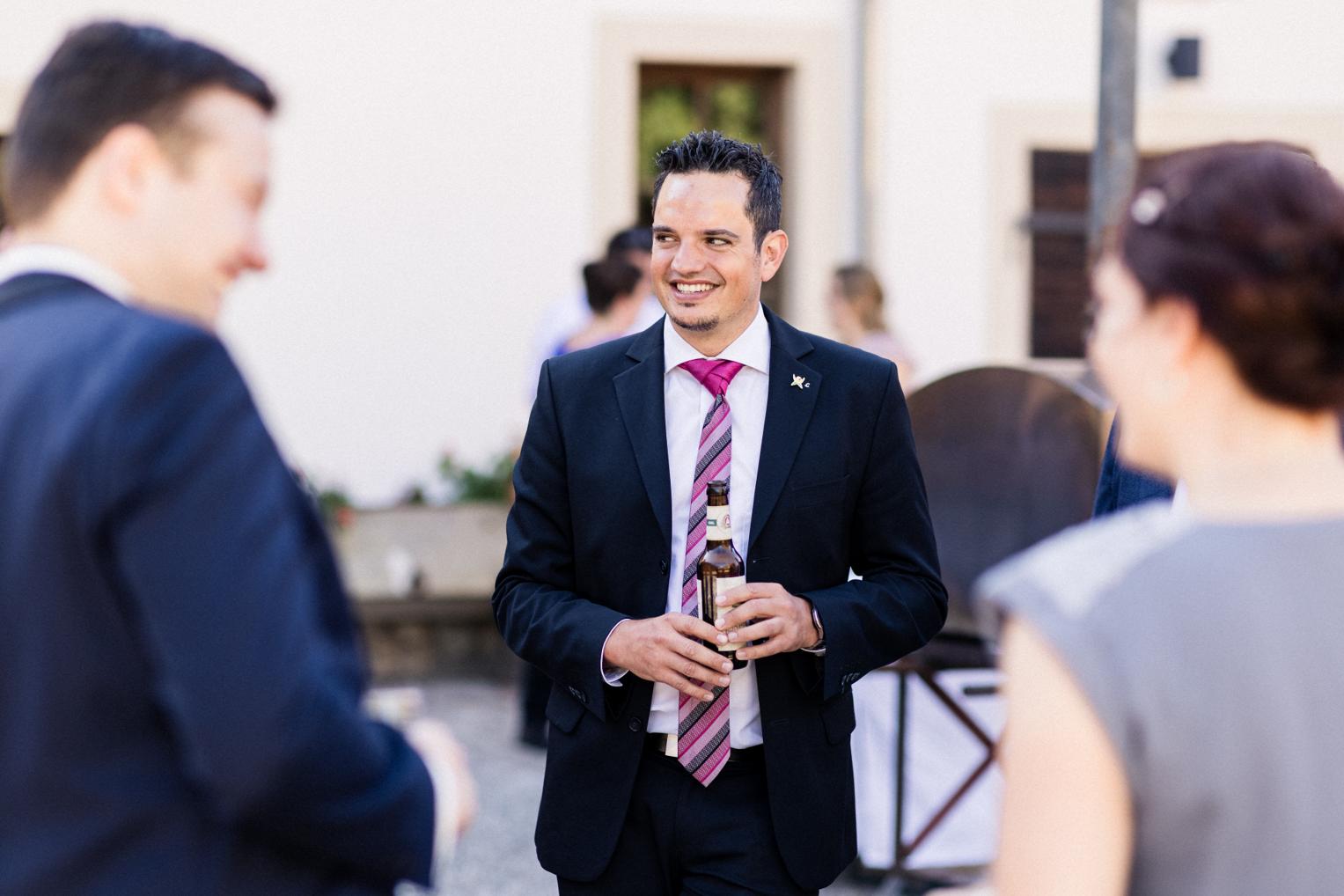 Hochzeitsgast lacht in pinker Krawatte mit Bier in der Hand
