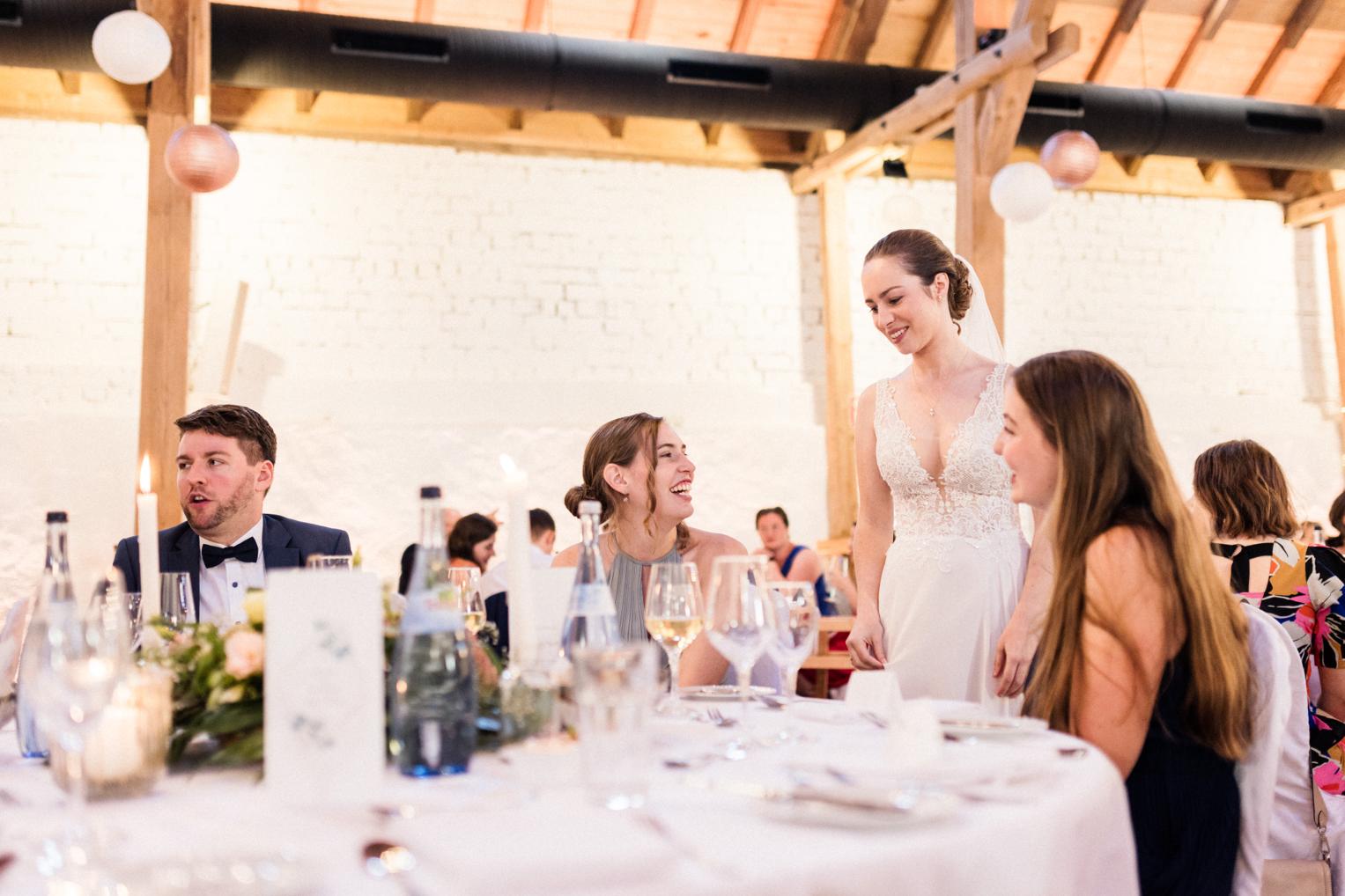 Braut spricht lachend mit Freundinnen am Hochzeitstisch