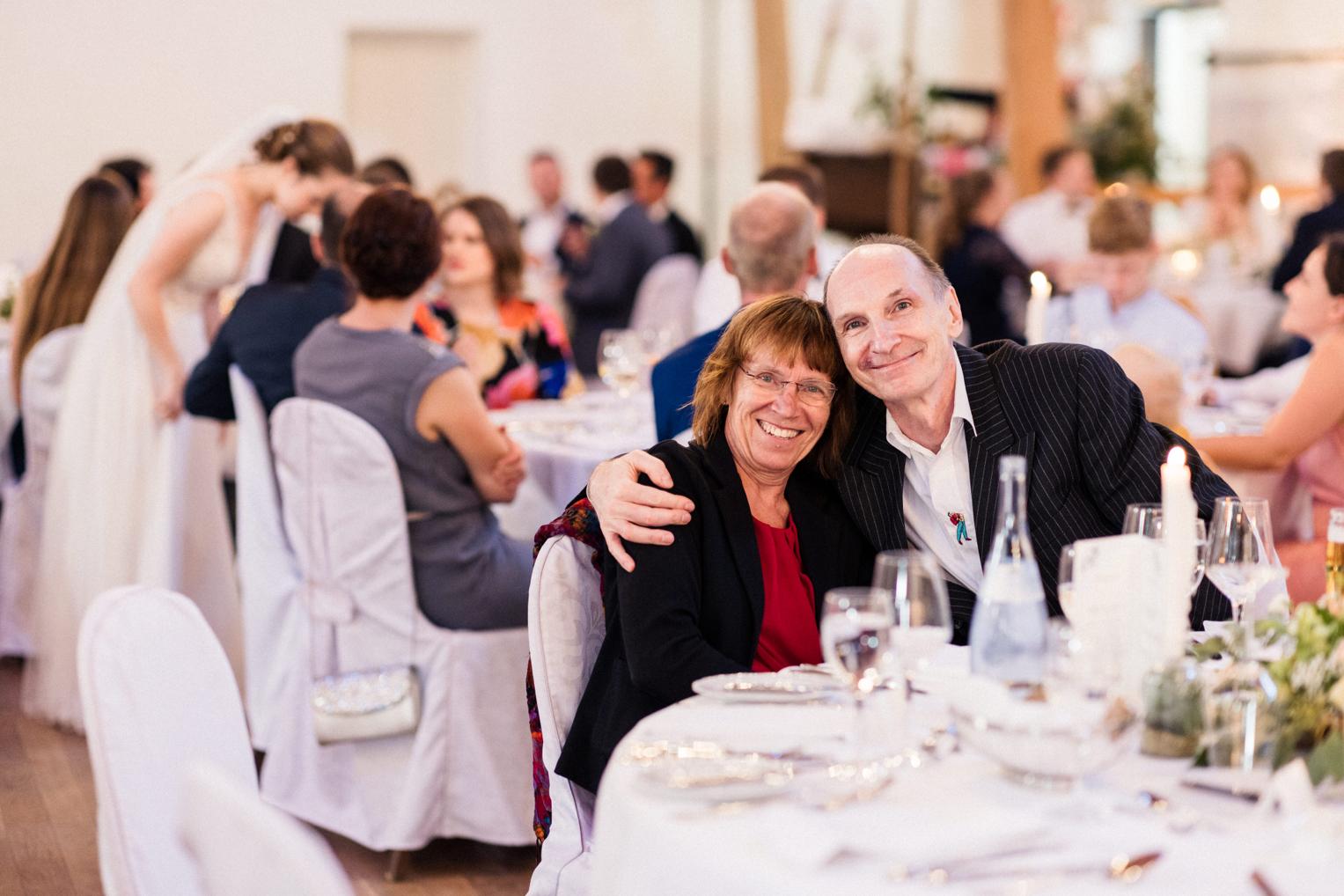 Älteres Hochzeitspaar lehnt sich liebevoll am Festtisch zusammen