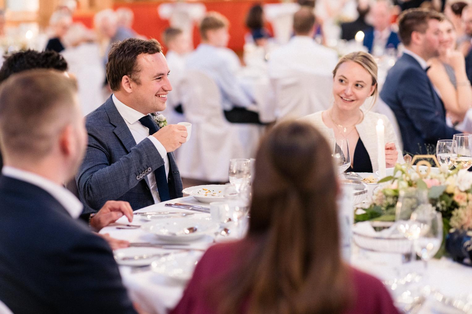 Brautpaar plaudert lachend mit Gästen am Hochzeitstisch