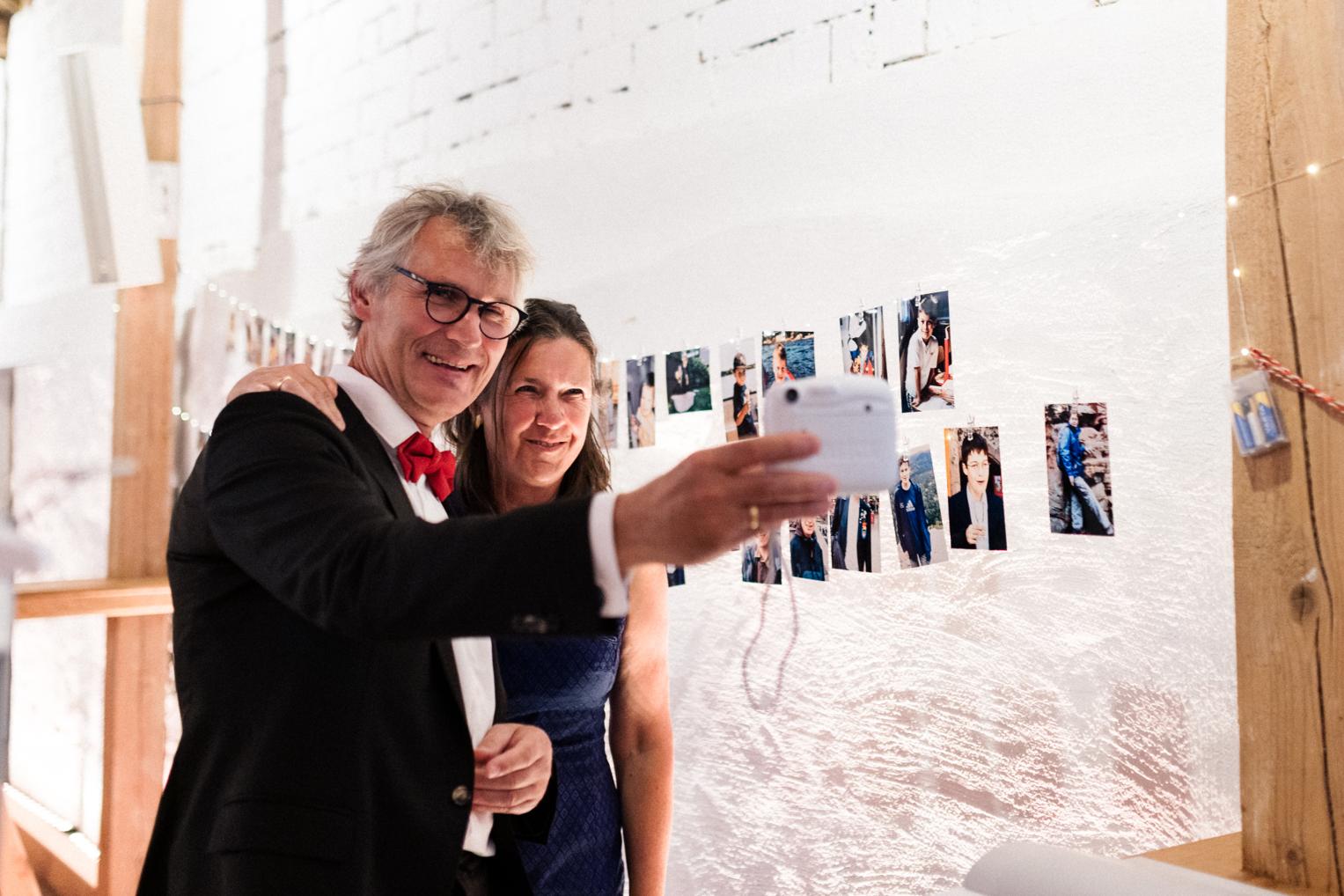 Hochzeitsgäste machen Selfie vor der Fotowand mit Kinderbildern