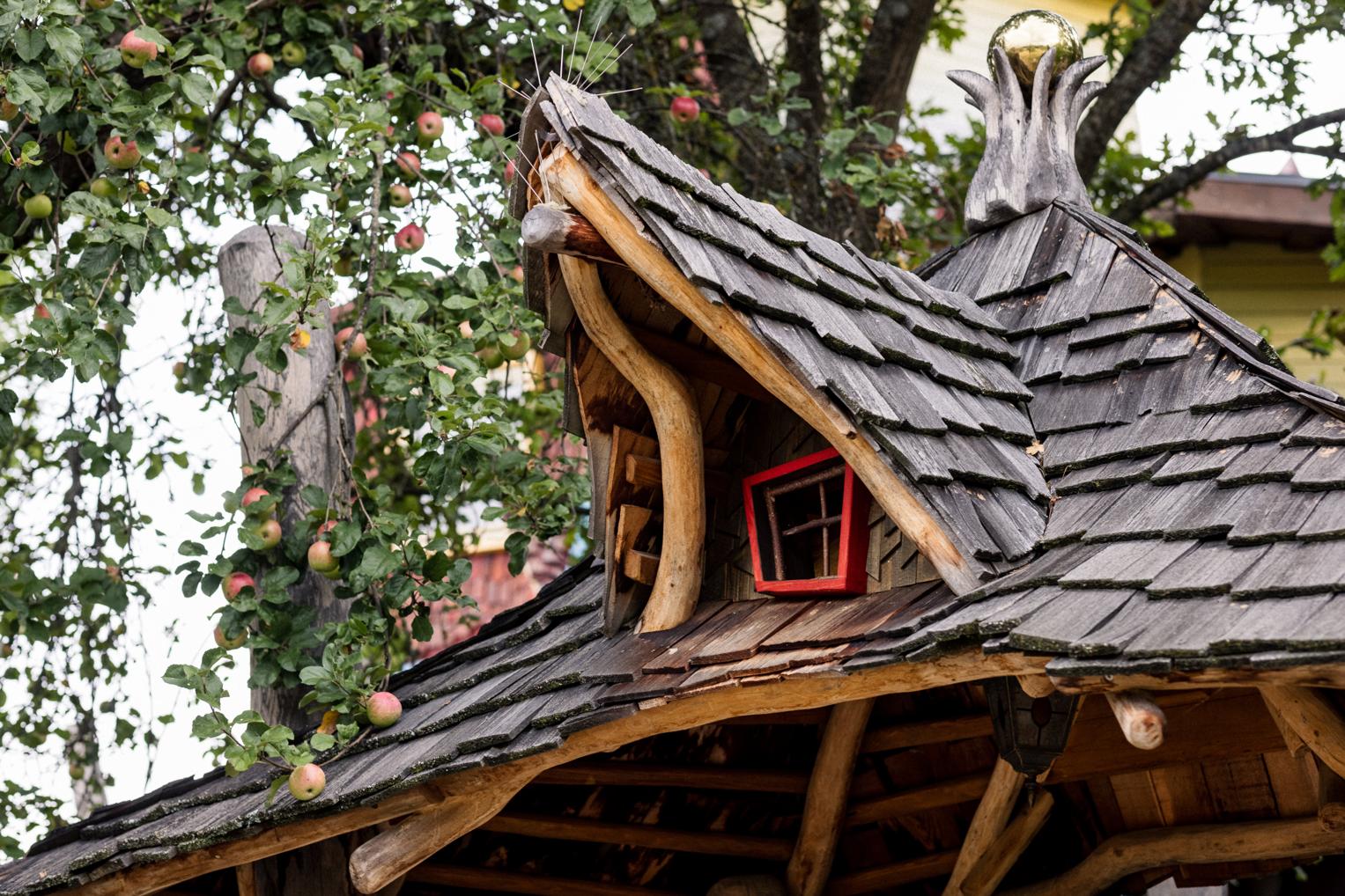 Detailaufnahme des verschnörkelten Holzdachs eines Baumhauses mit rotem Fenster