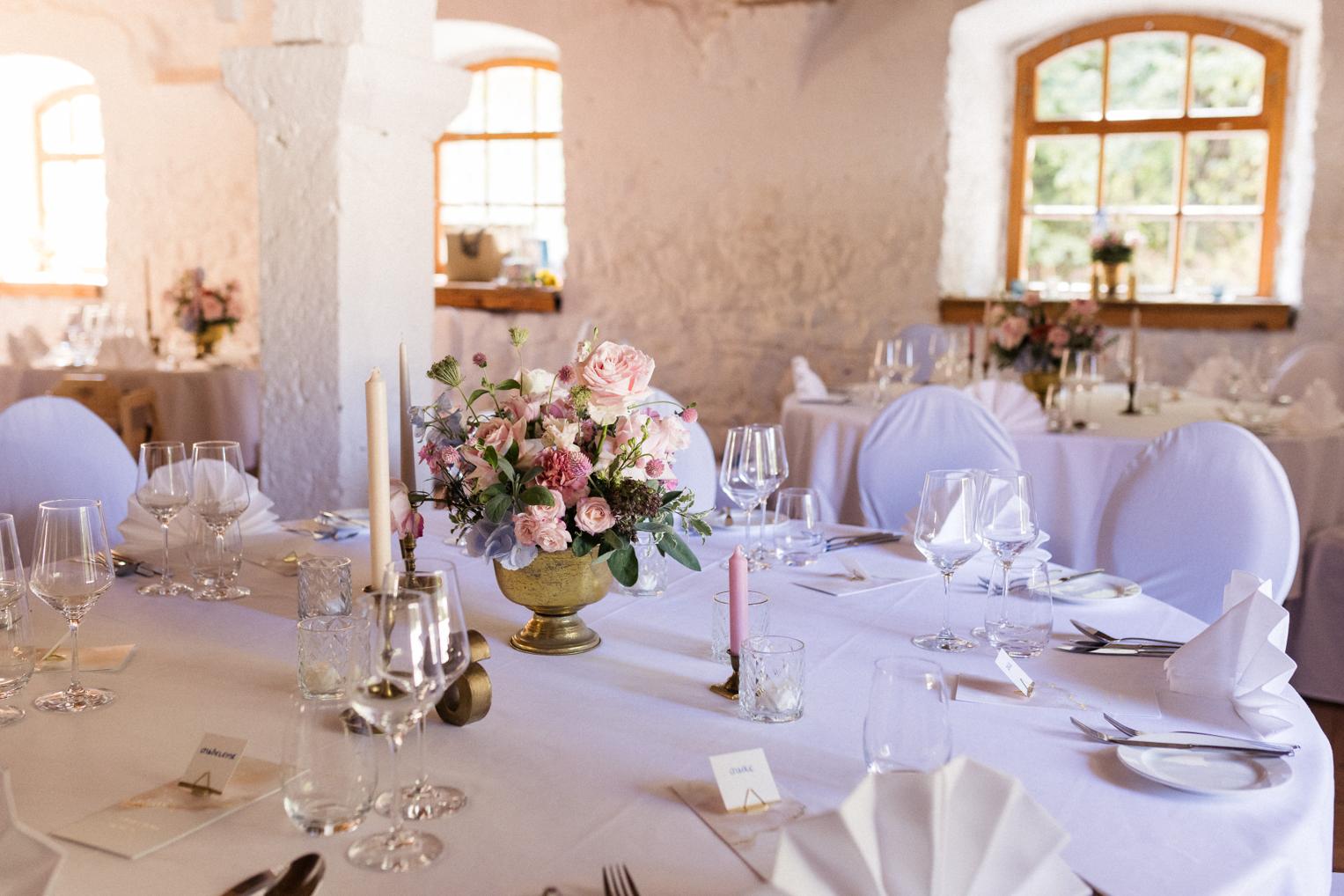 Tischdeko im Saal Schloss Ehrenfels: rosa Rosen im goldenen Pokal, Kerzen und Weingläser