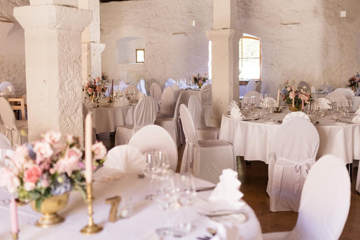 Gedeckter Bankettsaal Schloss Ehrenfels mit runden Tischen, Kerzen und Blumengestecken
