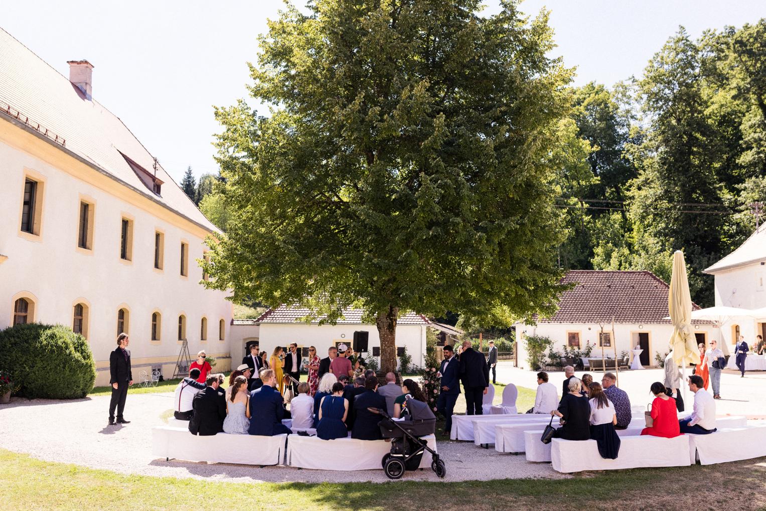 Freie Trauung im Innenhof Schloss Ehrenfels – Gäste sitzen im Kreis unter dem großen Baum