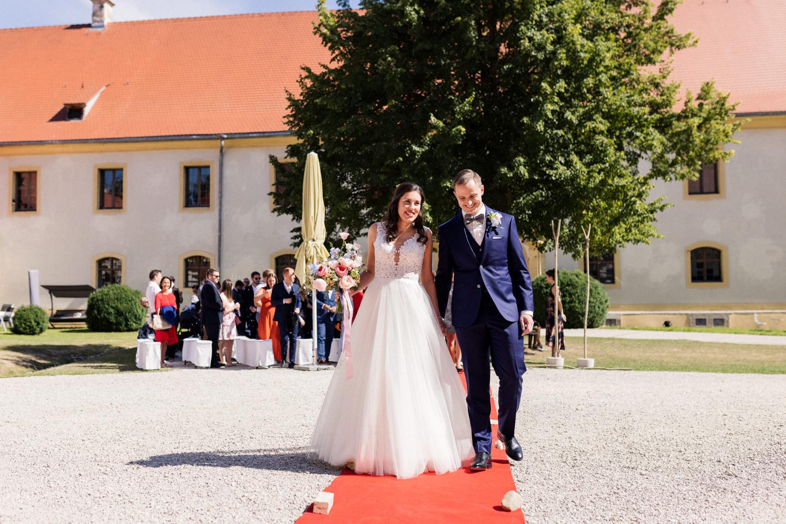 Brautpaar verlässt strahlend die Trauungsstätte über den roten Teppich, Schloss Ehrenfels