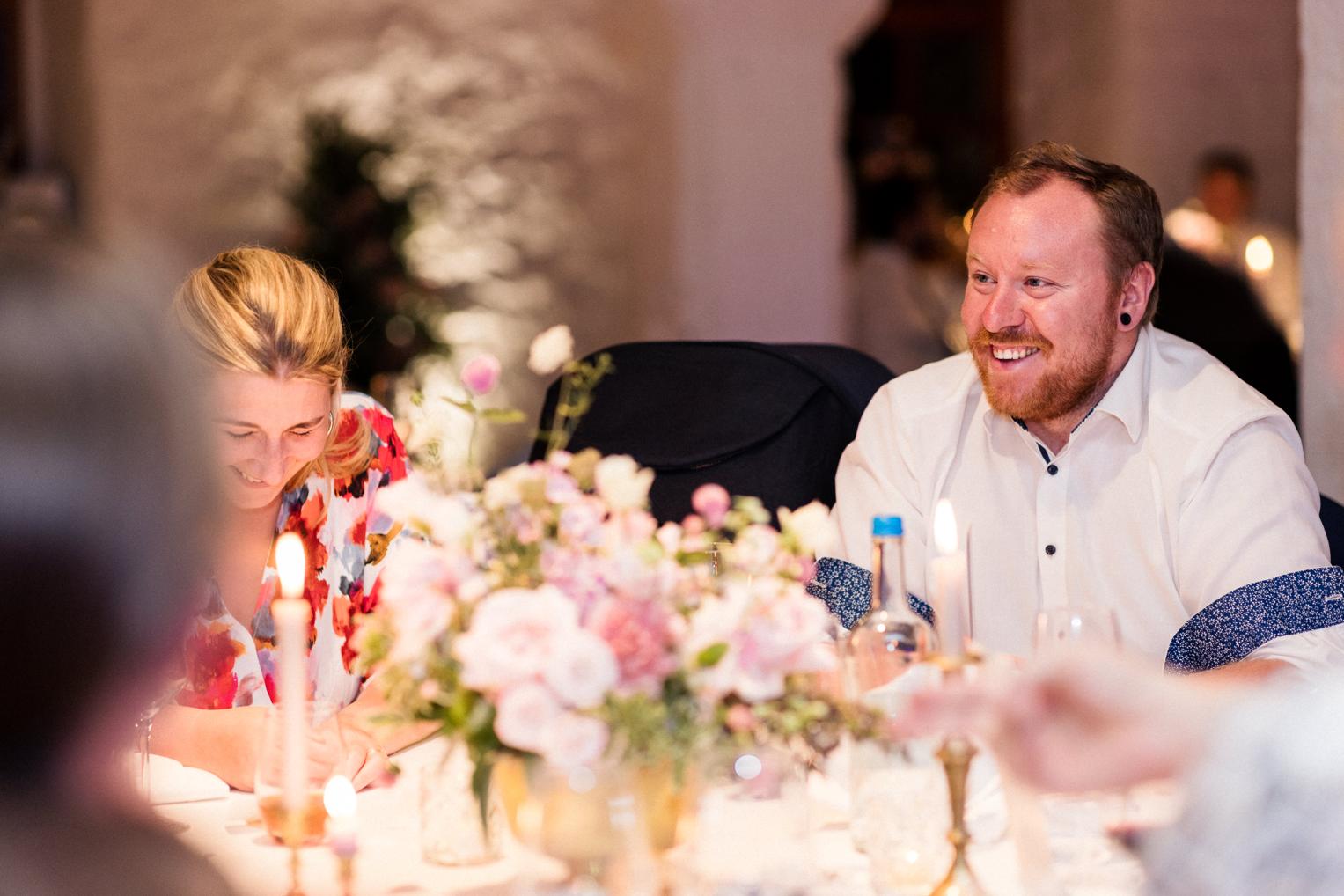 Gäste lachen ausgelassen beim abendlichen Dinner im Saal von Schloss Ehrenfels