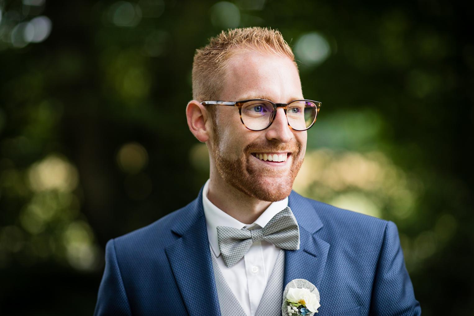 Lachendes Porträt des Bräutigams mit Brille und Fliege