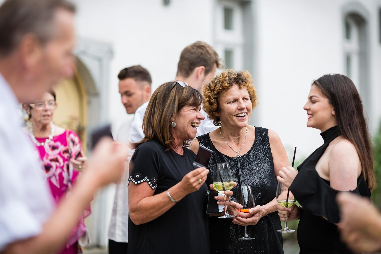 Hochzeitsgäste lachen herzlich beim Sektempfang im Innenhof