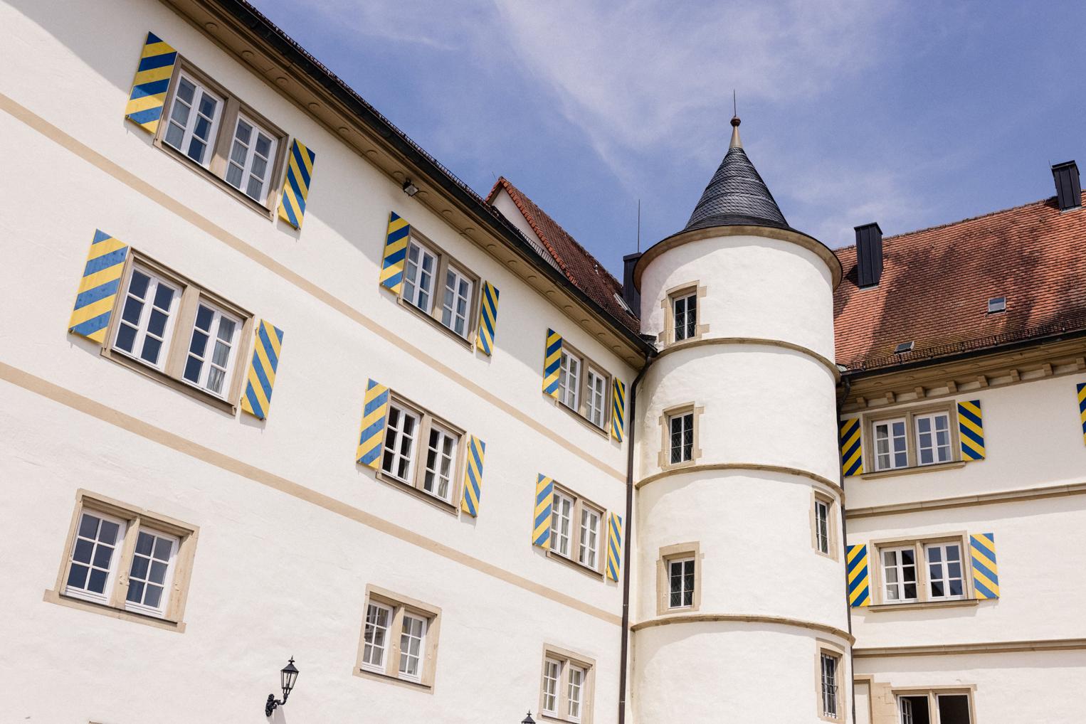 Schlossfassade mit blau-gelb gestreiften Fensterläden und spitzem Rundturm – Detail der Hochzeitslocation im Kraichgau