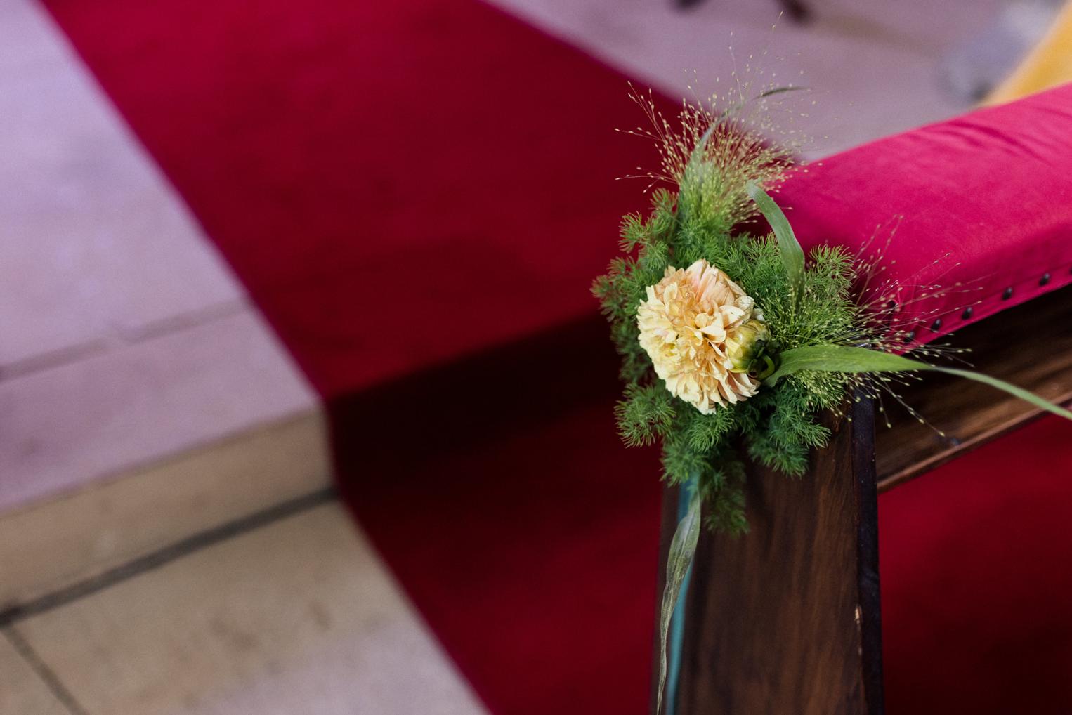 Blumenschmuck aus Dahlie und Gräsern am Ende einer Kirchenbank, dahinter der rote Teppich des Mittelgangs