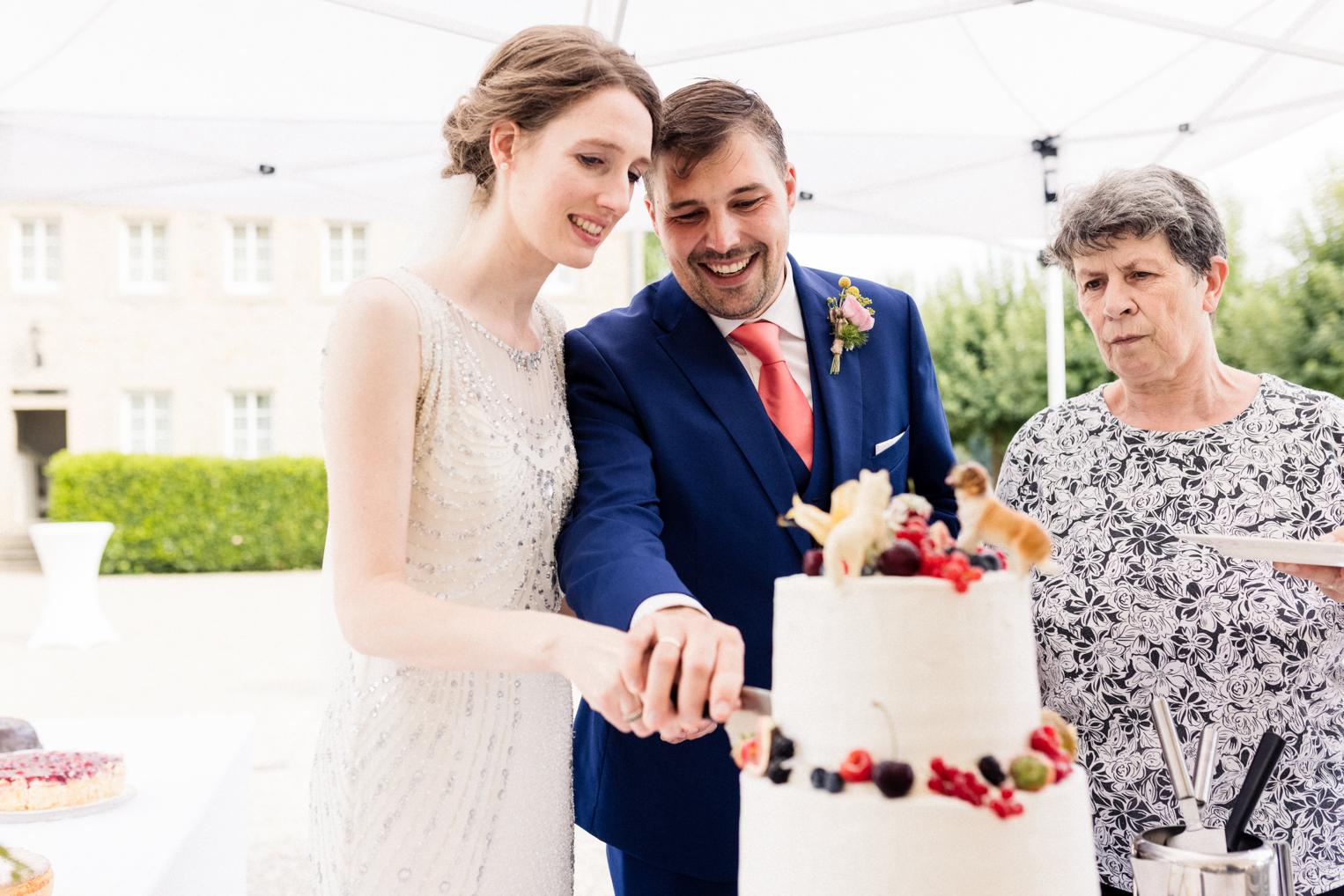Brautpaar schneidet gemeinsam die Hochzeitstorte an – unter dem Pavillonzelt im Hof von Schloss Neuhaus