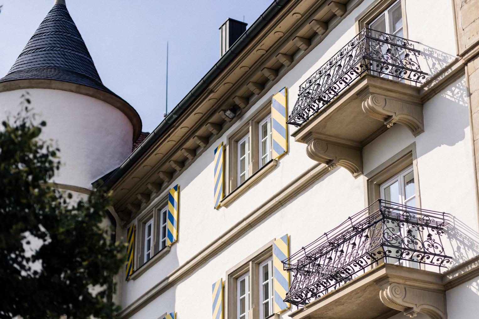 Schmiedeeiserne Balkone und blau-gelb gestreifte Läden an der Schlossfassade – architektonisches Detail der Location