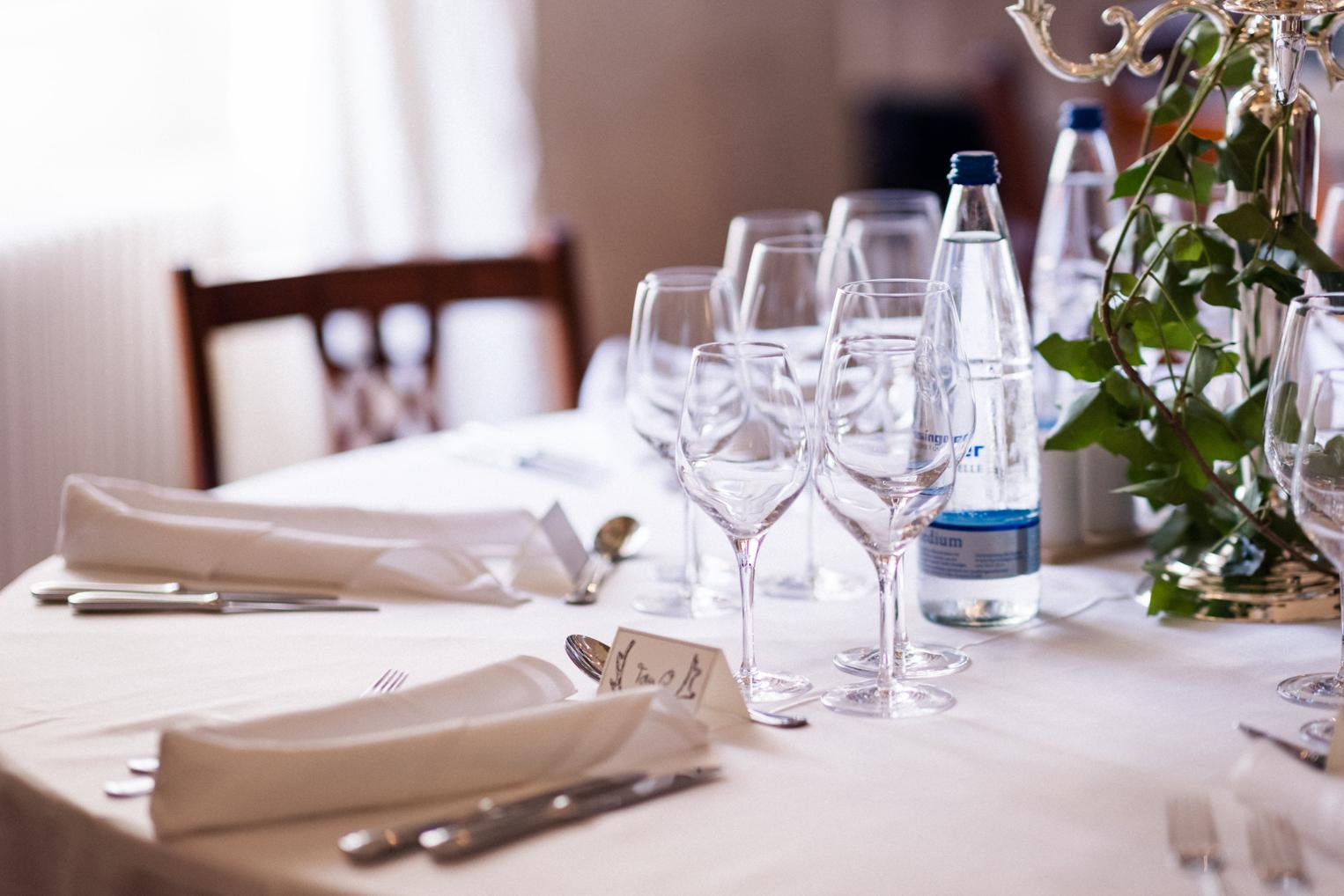 Gedeckter Tisch mit Weingläsern, Leinenservietten und handgeschriebener Tischkarte – Detail der Hochzeitstafel