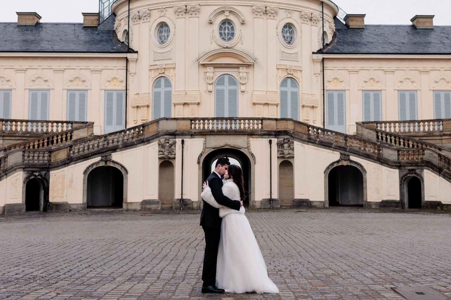 Bräutigam und Braut umarmen sich eng vor dem dunklen Torbogen von Schloss Solitude