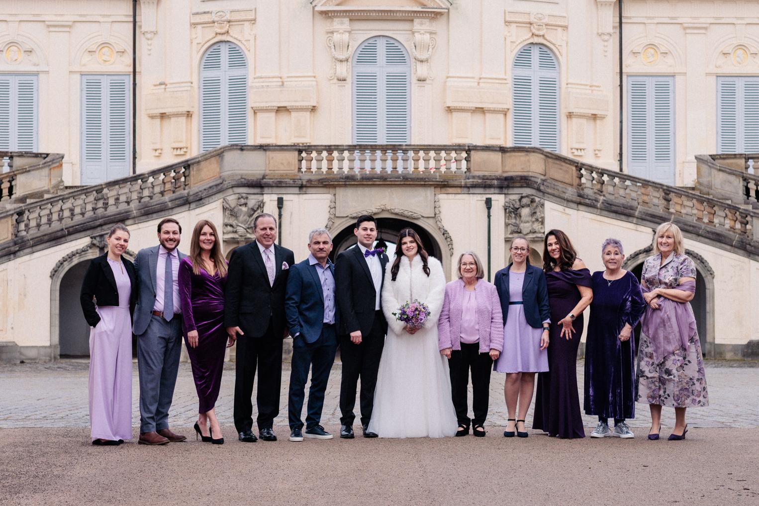 Familien-Gruppenfoto mit Brautpaar vor der Kuppel von Schloss Solitude, Gäste in violetten und lila Outfits