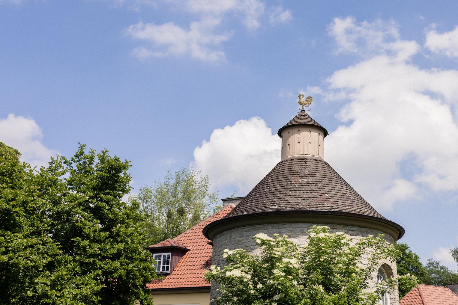 Turmzimmer der Villa Schwalbenhof in Gärtringen von außen – Schieferdach mit goldenem Wetterhahn, blauer Himmel