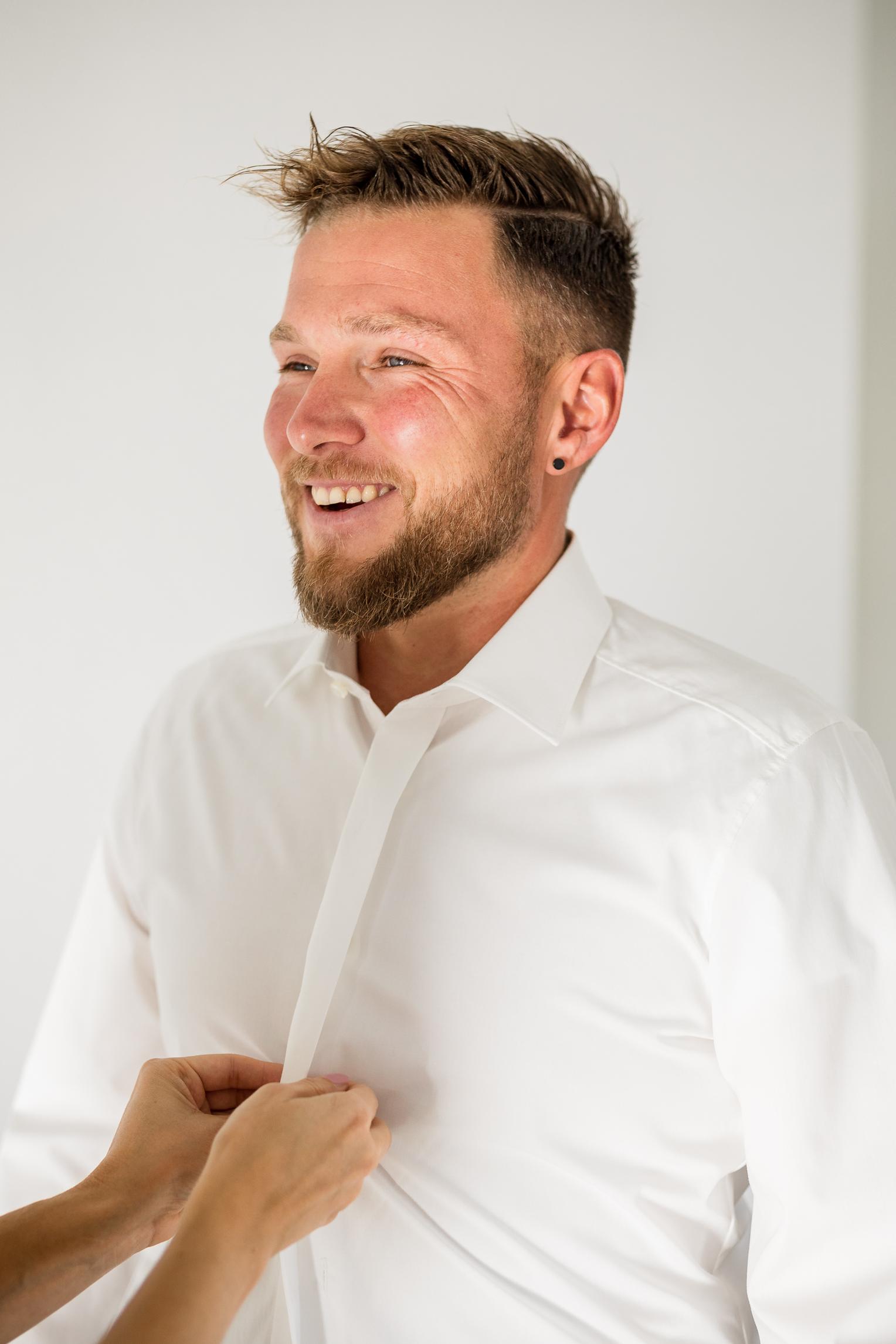 Getting Ready: Bräutigam lacht beim Anziehen des Hemdes, Hochzeit Kloster Kirchberg