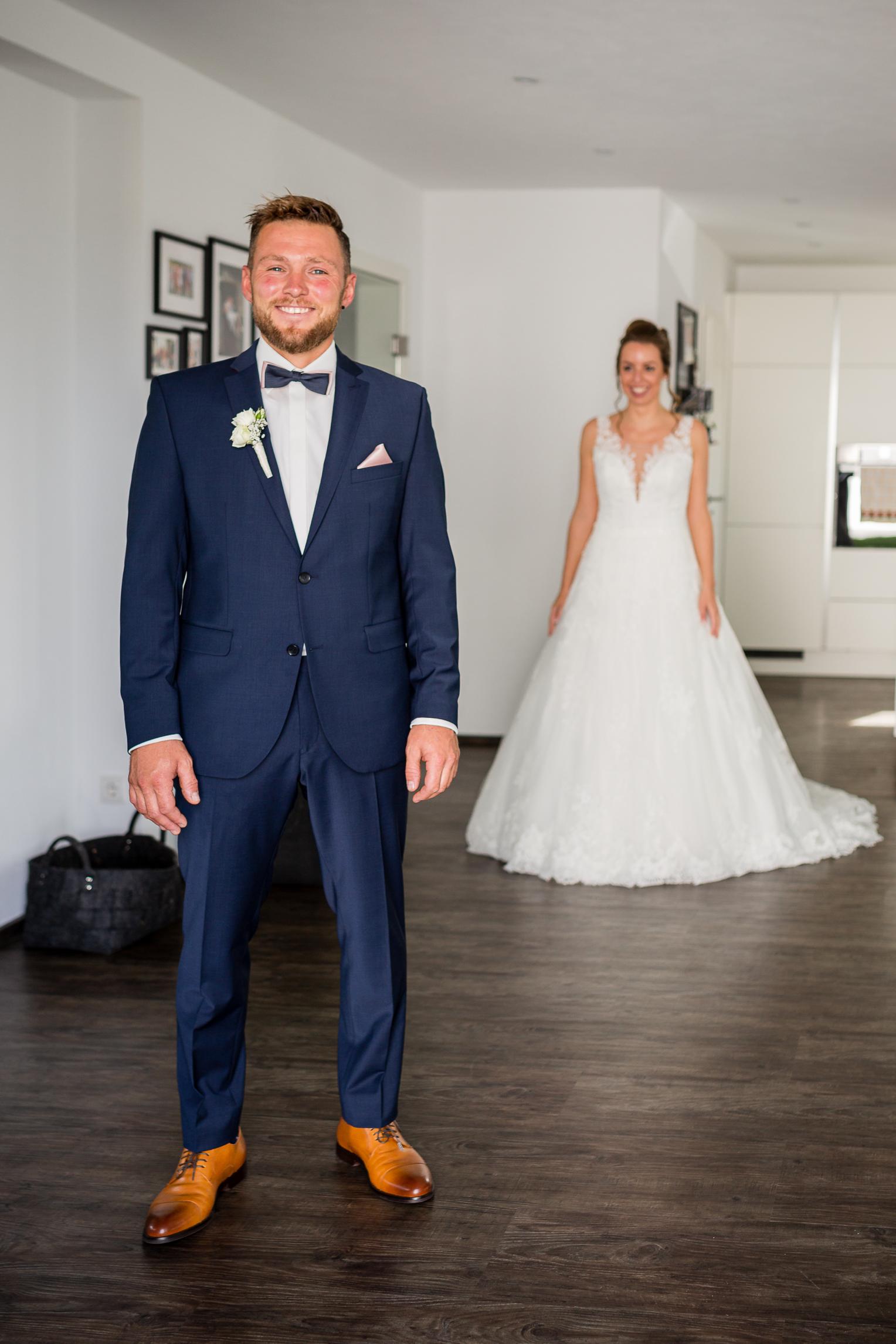 First Look zu Hause: Bräutigam im Anzug, Braut im Hintergrund nähert sich