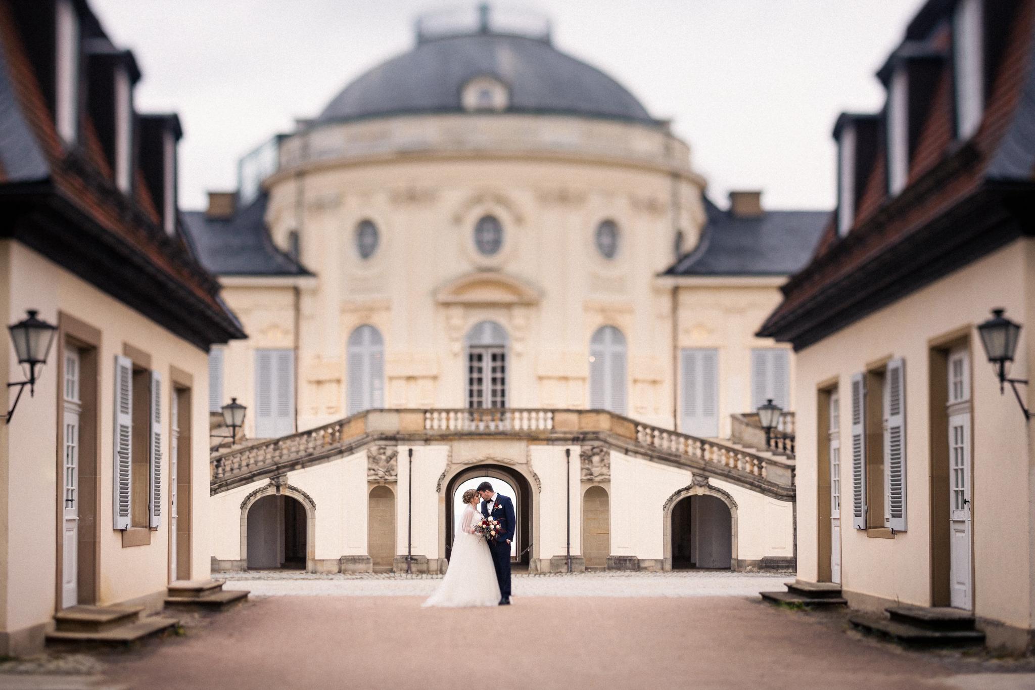 Brautpaar im Torbogen des Schloss Solitude, umgeben von historischer Architektur.