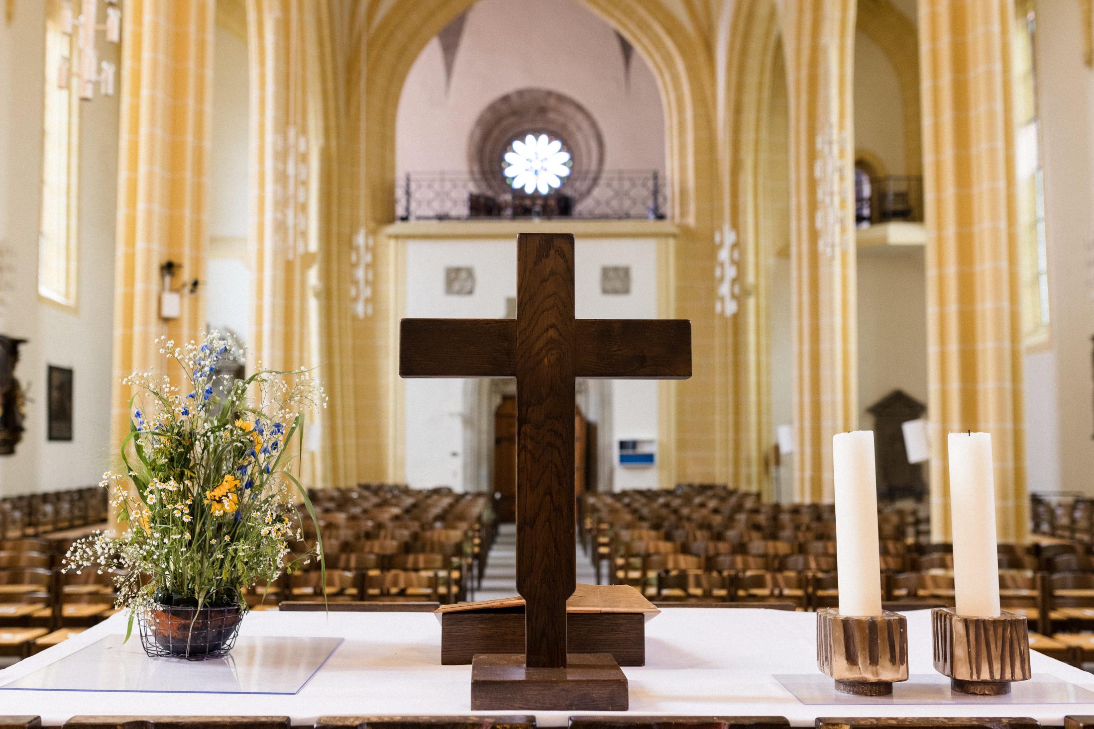 Altar der Stiftskirche in Herrenberg mit einem Holzkreuz und Kerzen, umgeben von Blumenarrangements.