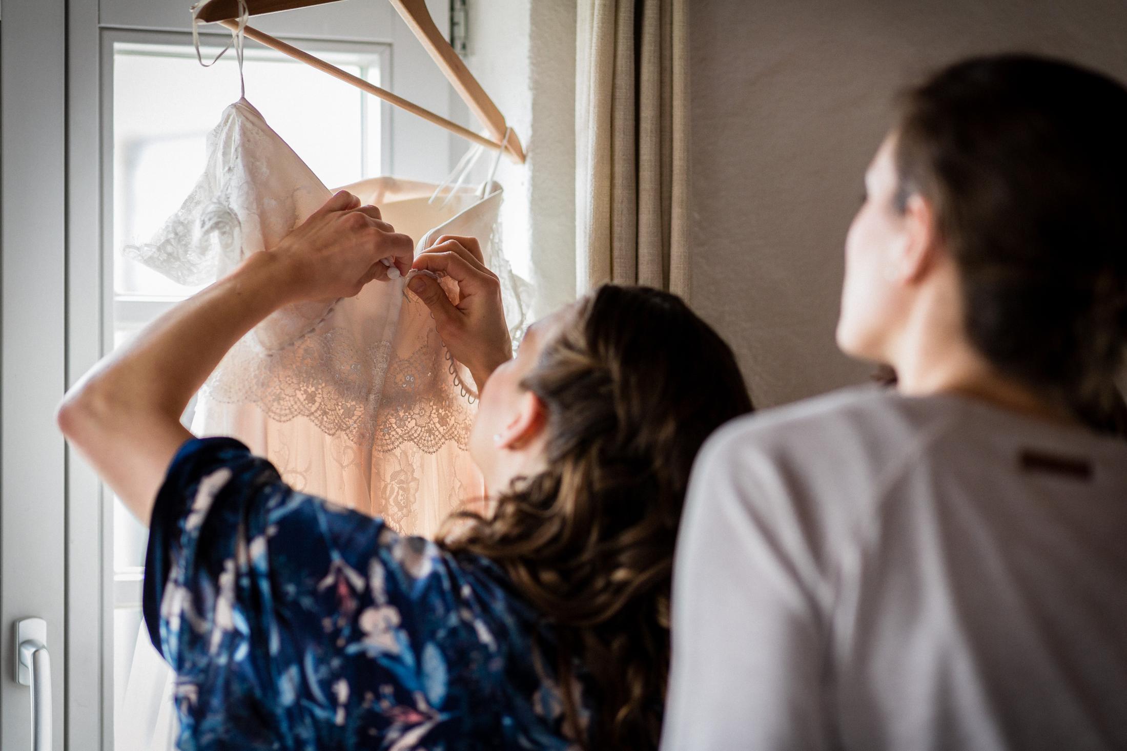 Trauzeuginnen nehmen das Brautkleid vorsichtig vom Bügel
