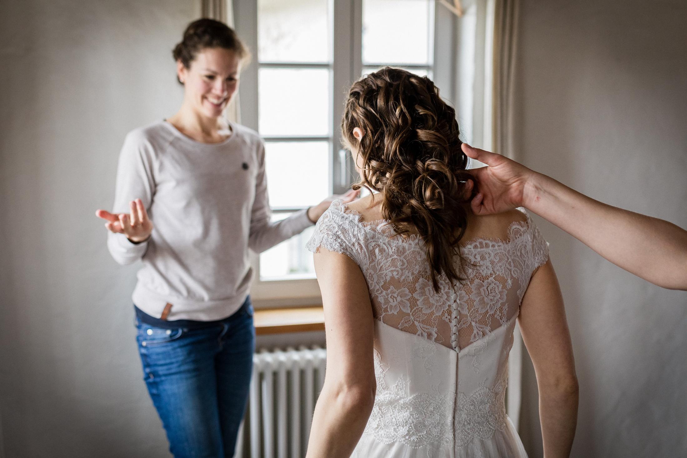 Braut im fertigen Kleid wird von Trauzeugin bewundert