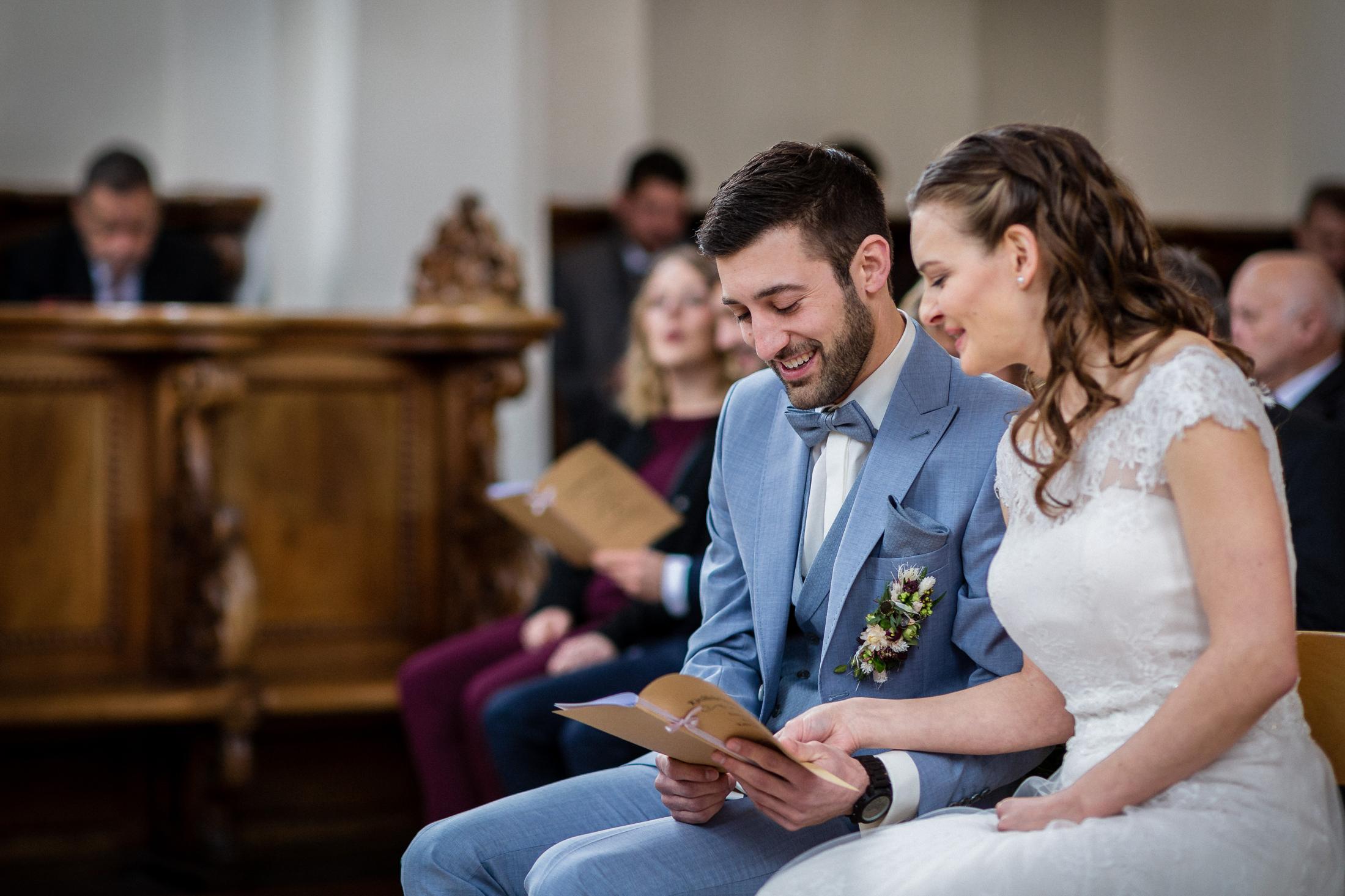 Brautpaar lacht während es das Liedheft in der Kirche liest