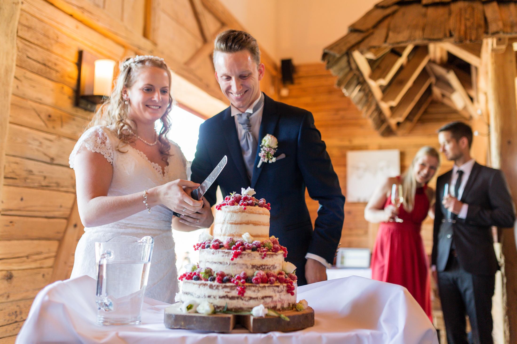 Brautpaar schneidet gemeinsam die Hochzeitstorte mit Beeren an