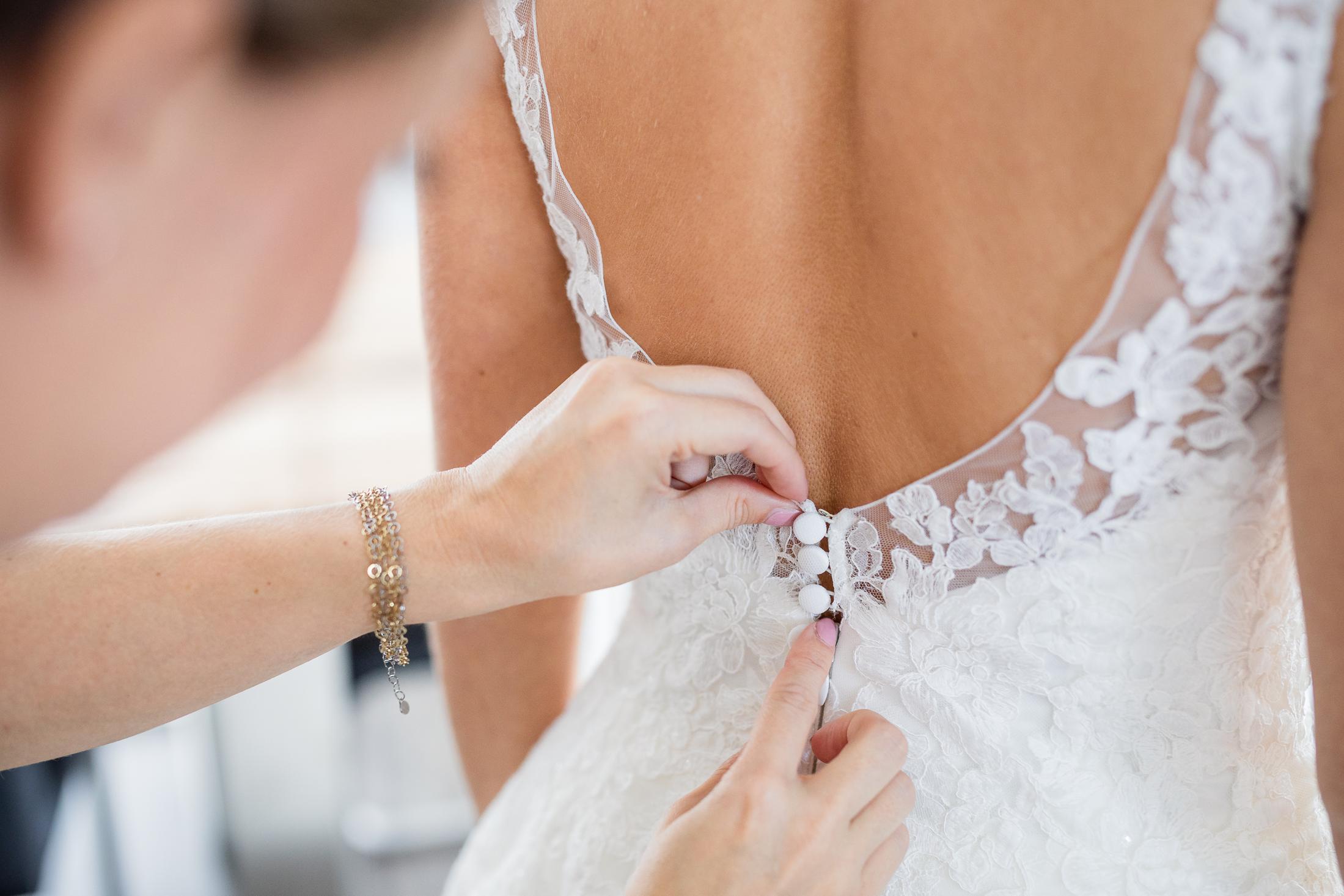 Getting Ready: Brautkleid wird der Braut am Rücken zugeknöpft, Spitzendetail