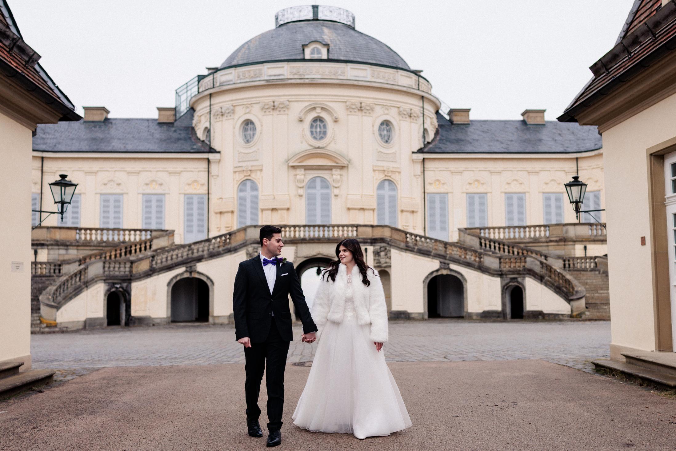 Brautpaar geht Hand in Hand über den Vorplatz von Schloss Solitude, im Hintergrund die geschwungene Freitreppe
