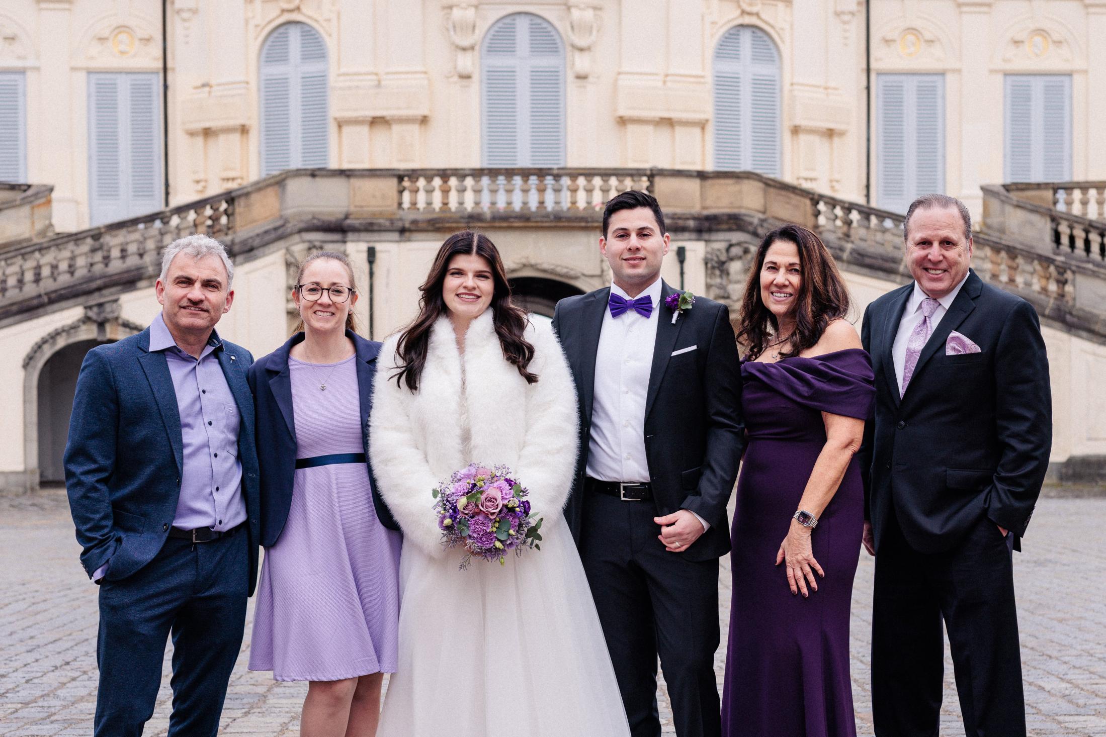 Gruppenfoto von Braut, Bräutigam und Familie vor der Freitreppe von Schloss Solitude, alle in Lila- und Violetttönen gekleidet