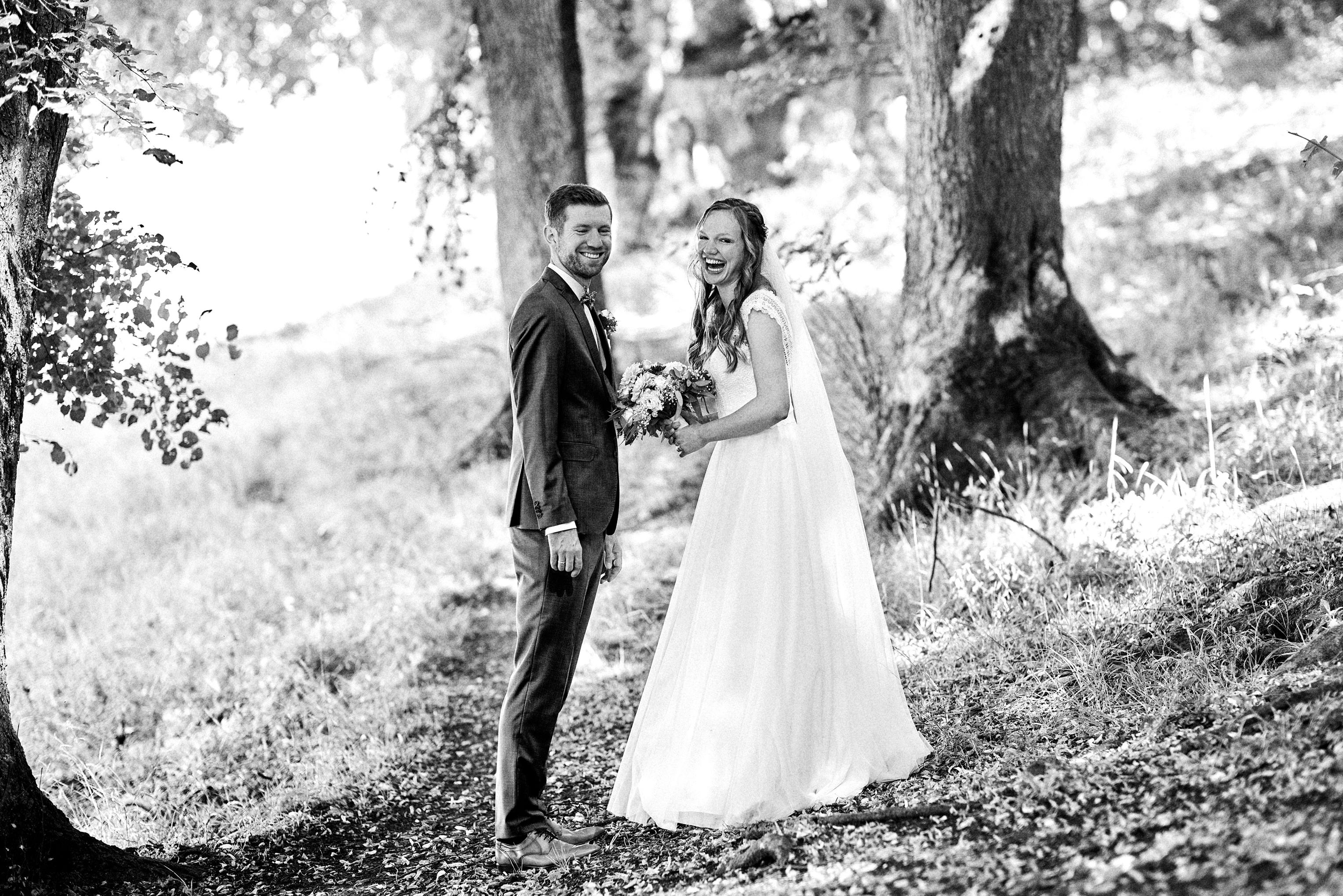Brautpaar lacht herzlich beim First Look am Waldrand