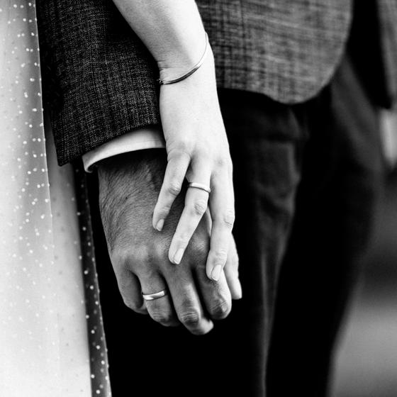 Nahaufnahme der ineinanderliegenden Hände von Braut und Bräutigam mit Eheringen während der Hochzeit