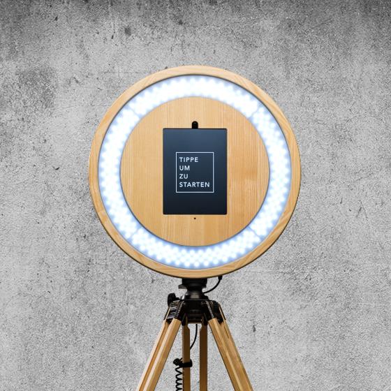 Lachendes Gästepaar mit Sonnenbrille und Hut vor einer hellen Fotobox-Wand auf einer Hochzeitsfeier