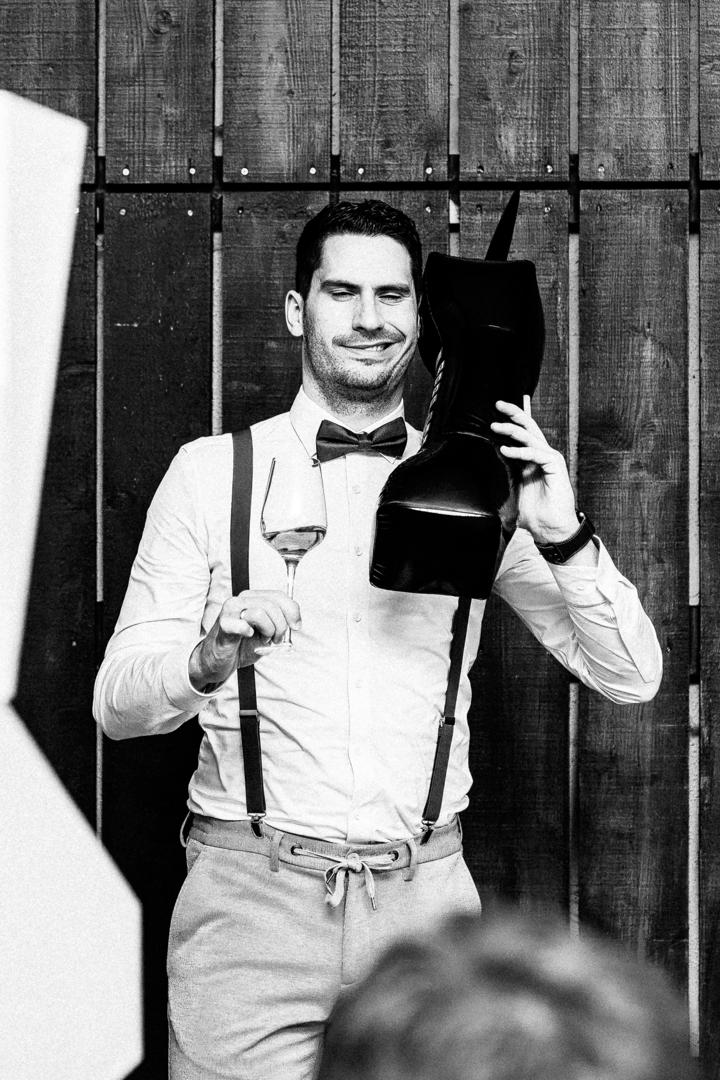 Gast bei der Hochzeitsfeier im Albgut Münsingen posiert humorvoll in der Fotobox mit einem aufblasbaren Stiefel und einem Glas Roséwein.