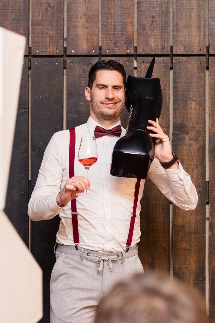 Gast bei der Hochzeitsfeier im Albgut Münsingen posiert humorvoll in der Fotobox mit einem aufblasbaren Stiefel und einem Glas Roséwein.